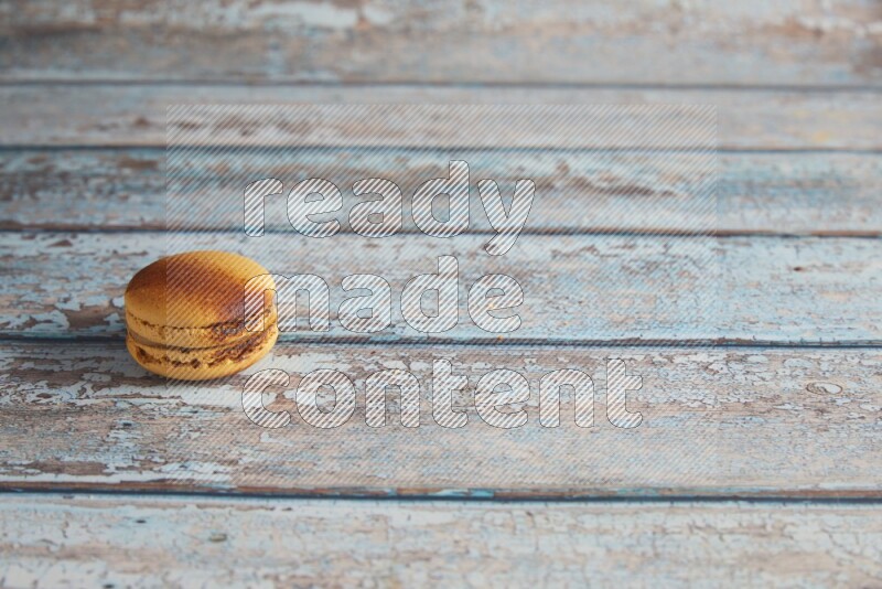 45º Shot of Yellow Crème Brulée macaron on light blue wooden background