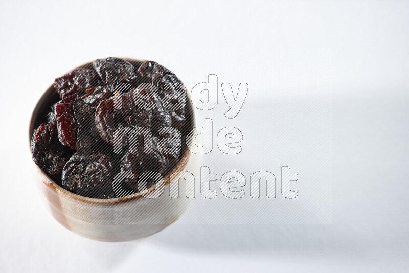 A beige ceramic bowl full of dried plums on a white background in different angles