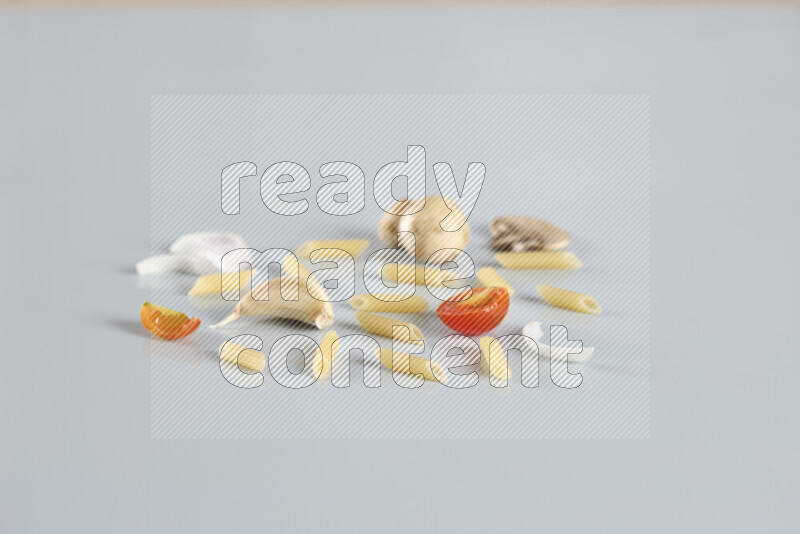 Raw pasta with different ingredients such as cherry tomatoes, garlic, onions, red chilis, black pepper, white pepper, bay laurel leaves, rosemary, cardamom and mushrooms on light blue background