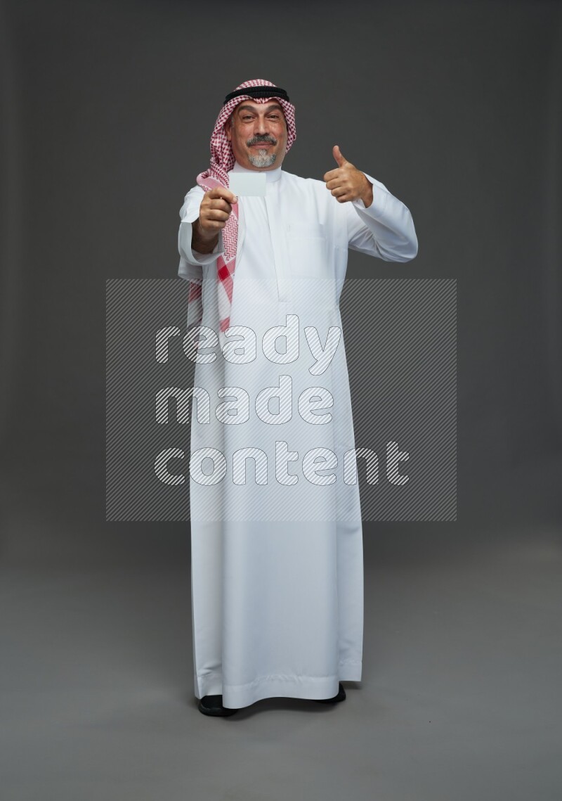 Saudi man with shomag Standing holding ATM card on gray background