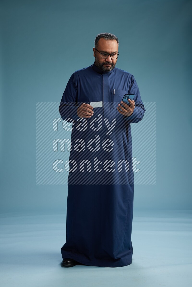 Saudi Man without shimag Standing holding ATM while talking on phone on blue background