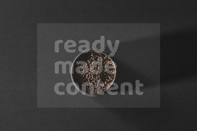 A black pottery bowl full of black pepper beads on black flooring