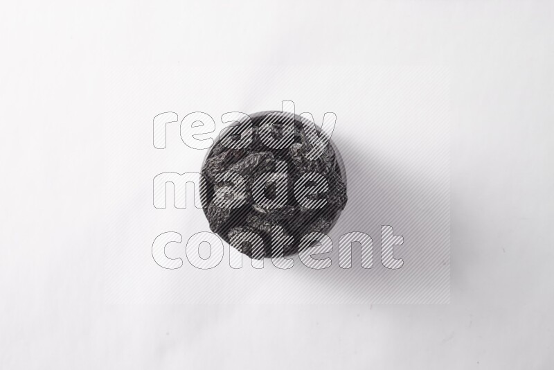 Dried plums in a black pottery bowl on white background