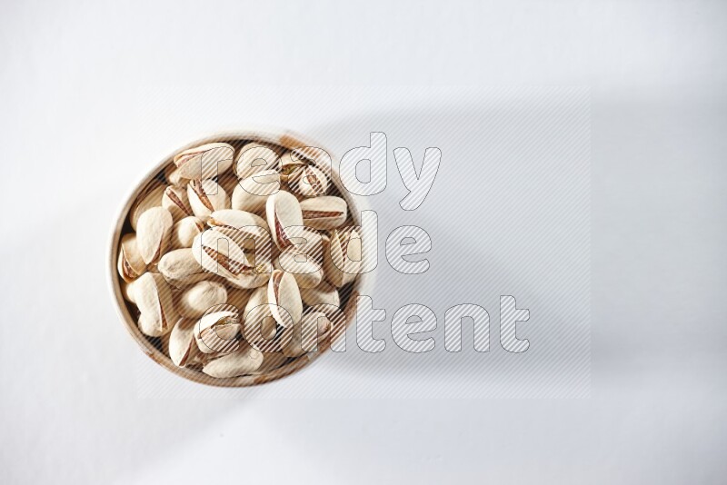 A beige ceramic bowl full of pistachios on a white background in different angles