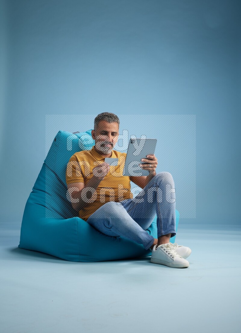 A man sitting on a blue beanbag and holding ATM card with tablet