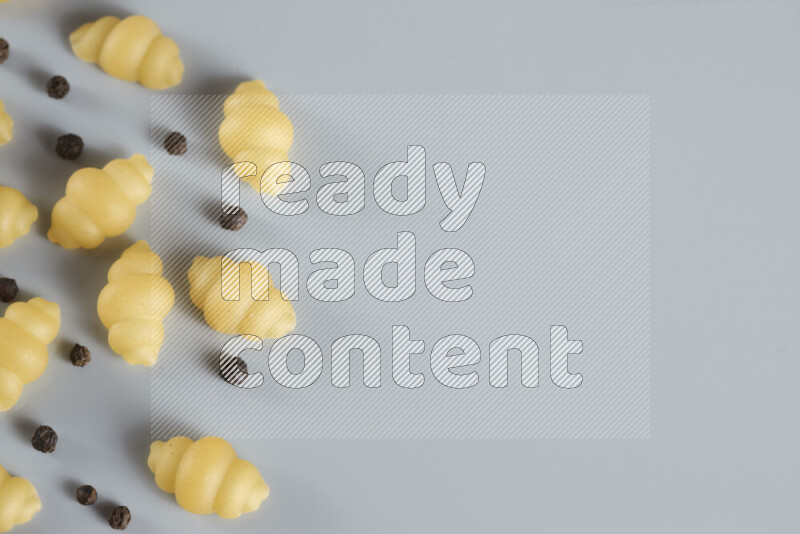 Raw pasta with different ingredients such as cherry tomatoes, garlic, onions, red chilis, black pepper, white pepper, bay laurel leaves, rosemary, cardamom and mushrooms on light blue background