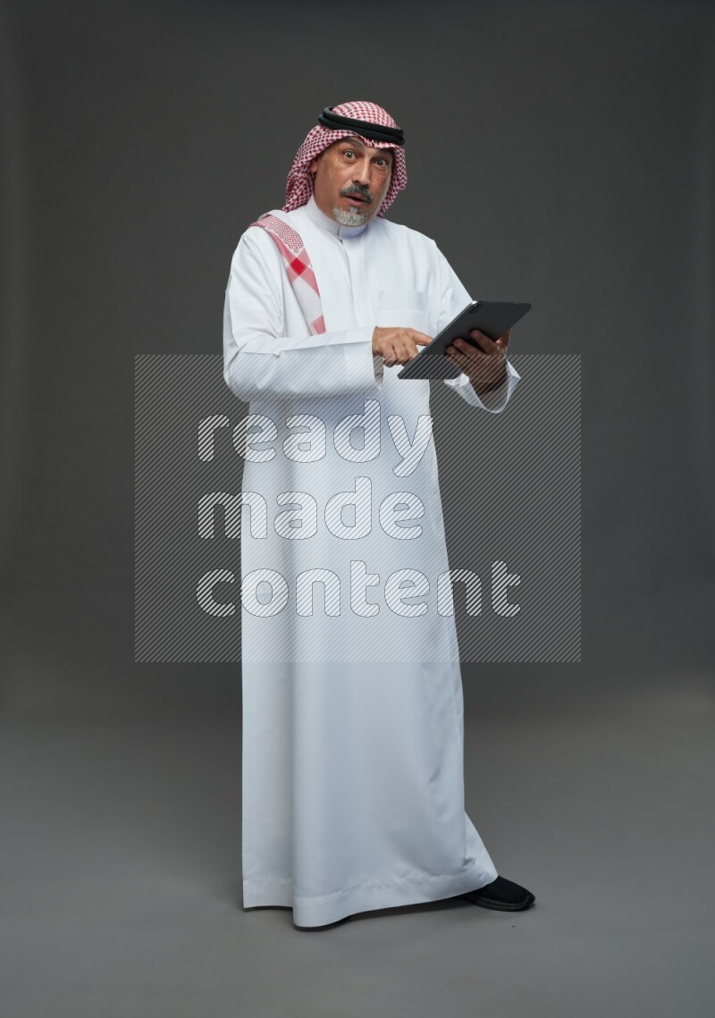 Saudi man with shomag Standing working on tablet on gray background