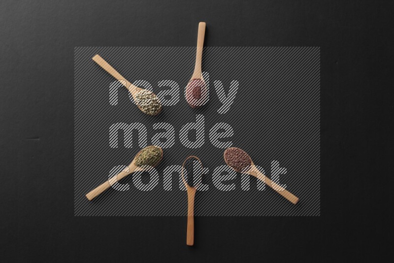 wooden spoons filled with white peppers, mustard seeds, black seeds, garden cress, cumin and flax on black flooring