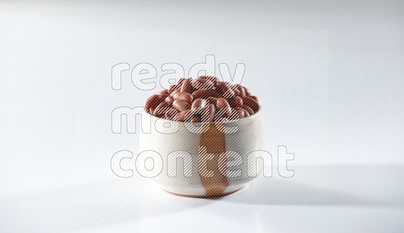 A beige ceramic bowl full of red skin peanuts on a white background in different angles