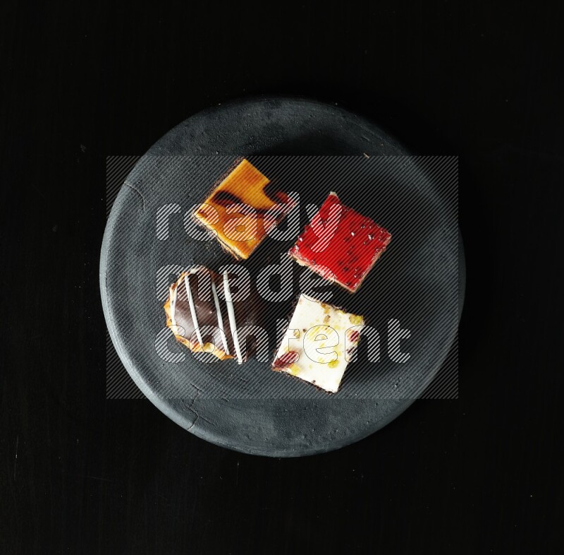 Assorted desserts in a black pottery plate on black background