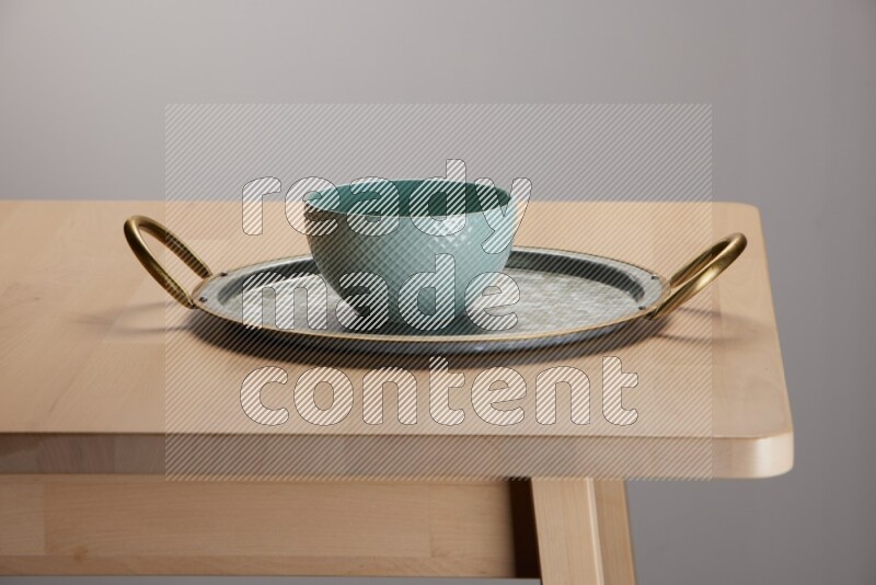 blue bowl placed on a rounded stainless steel metal tray with golden handels on the edge of wooden table
