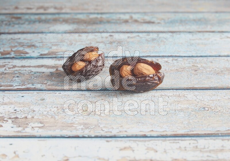 two almond stuffed madjoul dates on a light blue wooden background