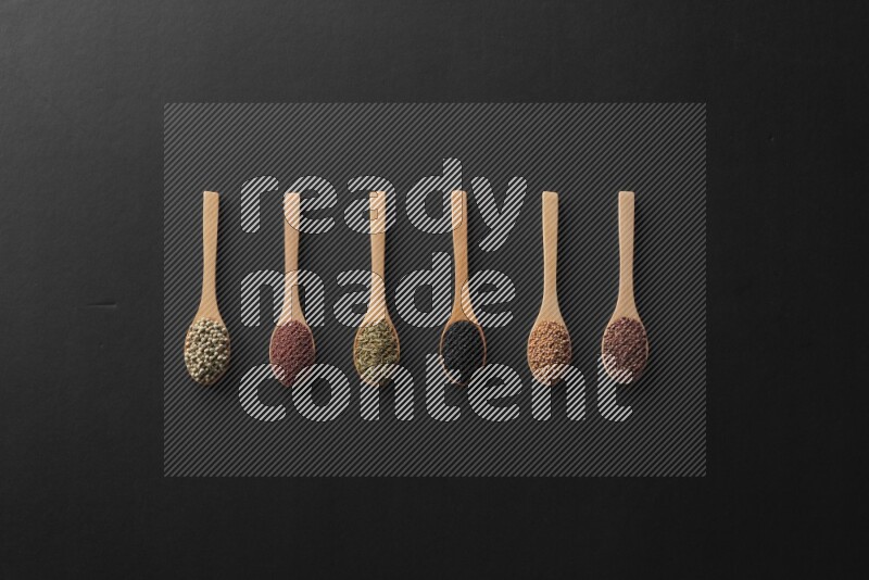 wooden spoons filled with white peppers, mustard seeds, black seeds, garden cress, cumin and flax on black flooring