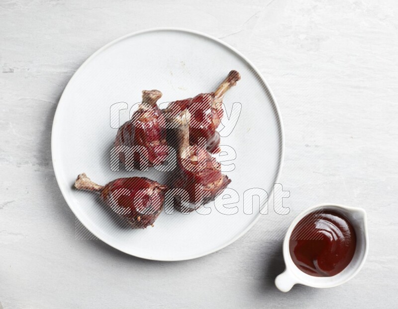 drumstick wrapped in bacon on round white ceramic plate on grey textured countertop