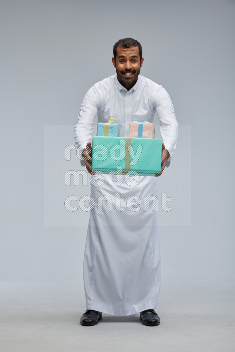 Saudi man Wearing thob standing holding gift box on Gray background