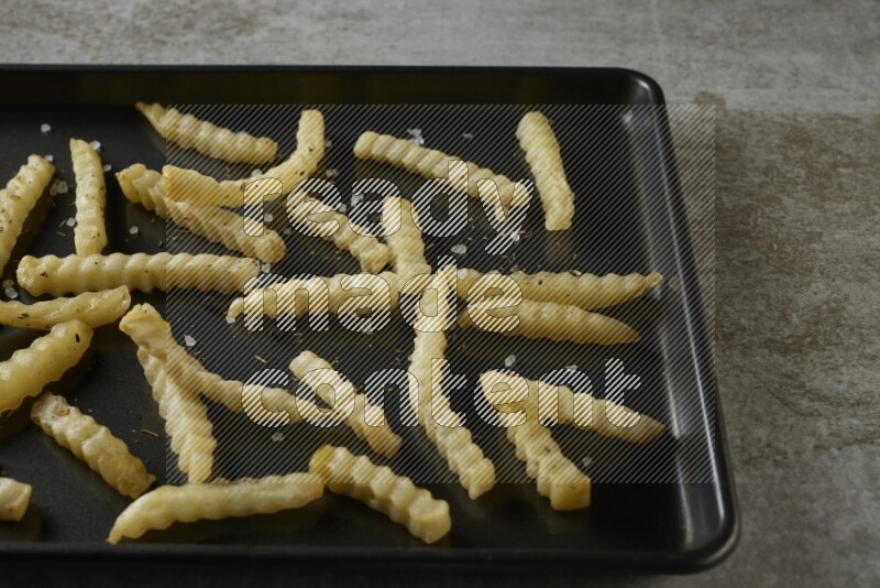 crinkle fries in a black stainless steel rectangle tray on grey textured counter top