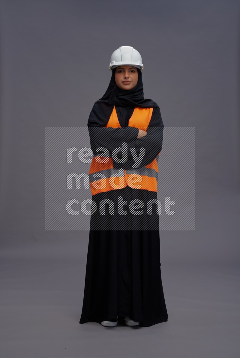 Saudi woman wearing Abaya with engineer vest standing with crossed arms on gray background