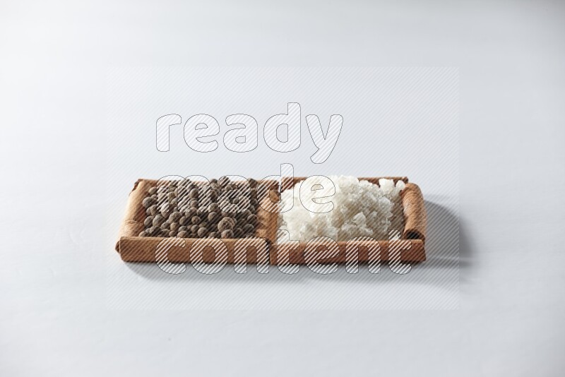 مربعان من أعواد القرفة ممتلئان بالملح الأبيض وحبوب الفلفل الحلو علي خلفية بيضاء