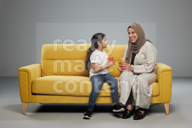 Mom and daughter sitting drinking juice on gray background