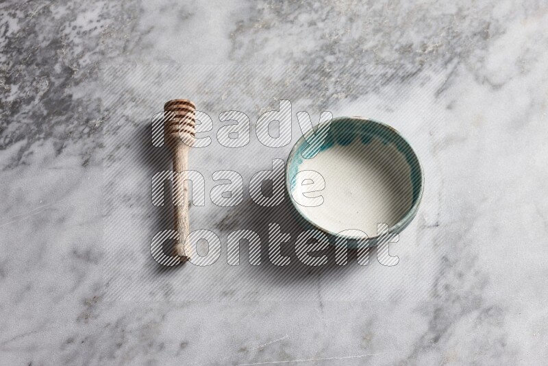 Multicolored pottery bowl with wooden honey dipper on the side on grey marble background