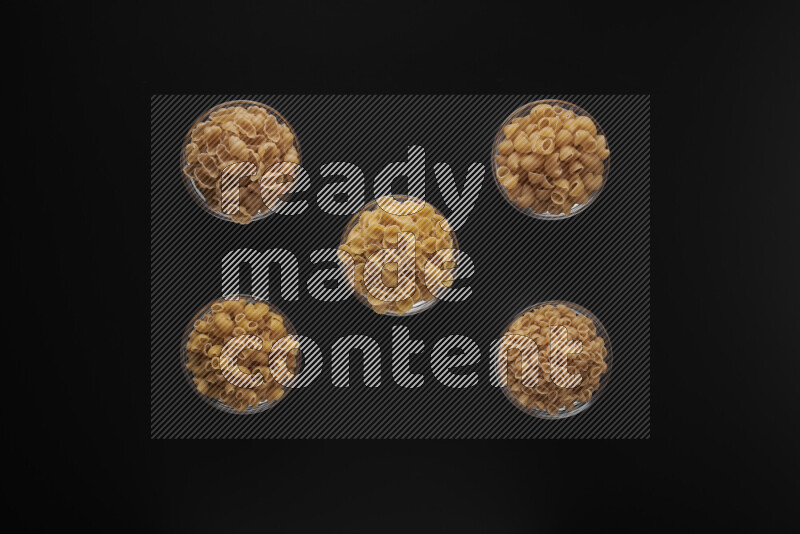 Different pasta types in 5 glass bowls on black background