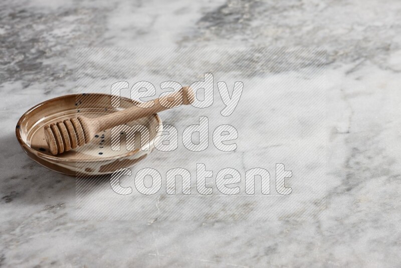 Multicolored pottery plate with wooden honey dipper in it on grey marble background