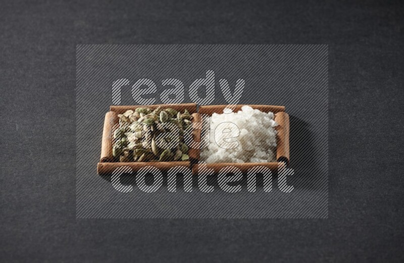 مربعان من أعواد القرفة ممتلئان بالملح الأبيض وحبوب الهيل علي خلفية سوداء