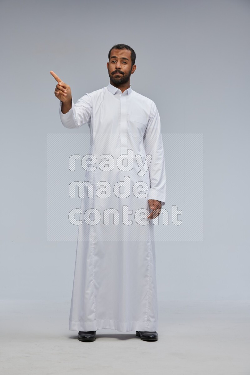 Saudi man Wearing Thob standing interacting with the camera on Gray background