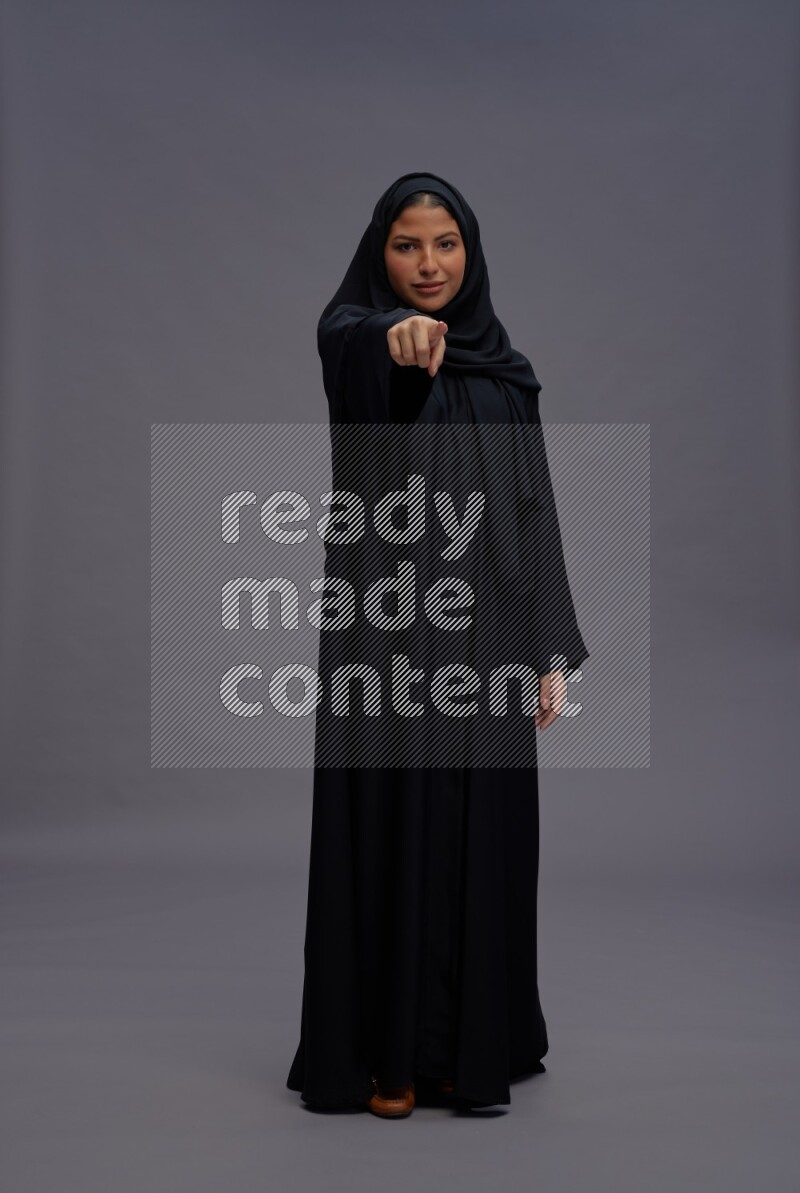 Saudi woman wearing Abaya standing interacting with the camera on gray background