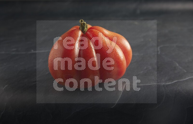 45 degree single heirloom tomato on a textured black slate background