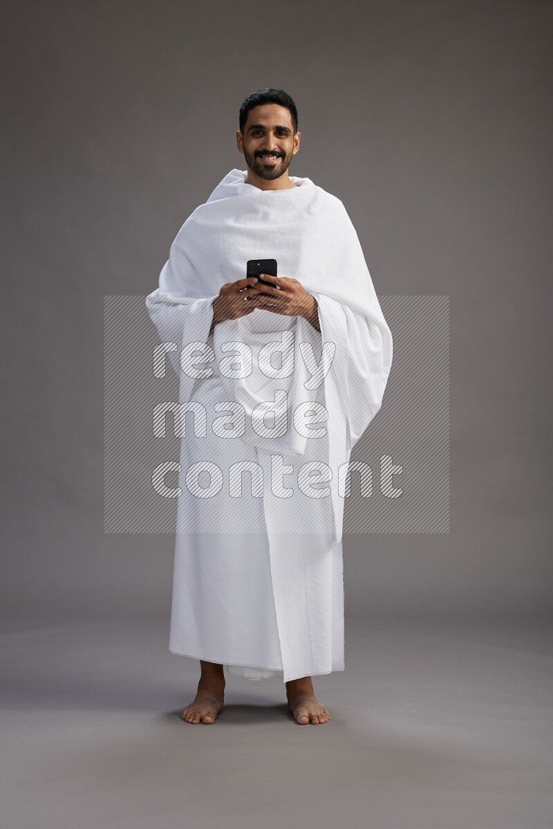 A man wearing Ehram Standing texting on phone on gray background