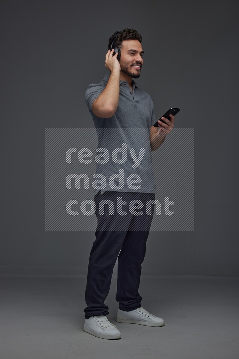 A man wearing casual and using his phone and headphone eye level on a gray background