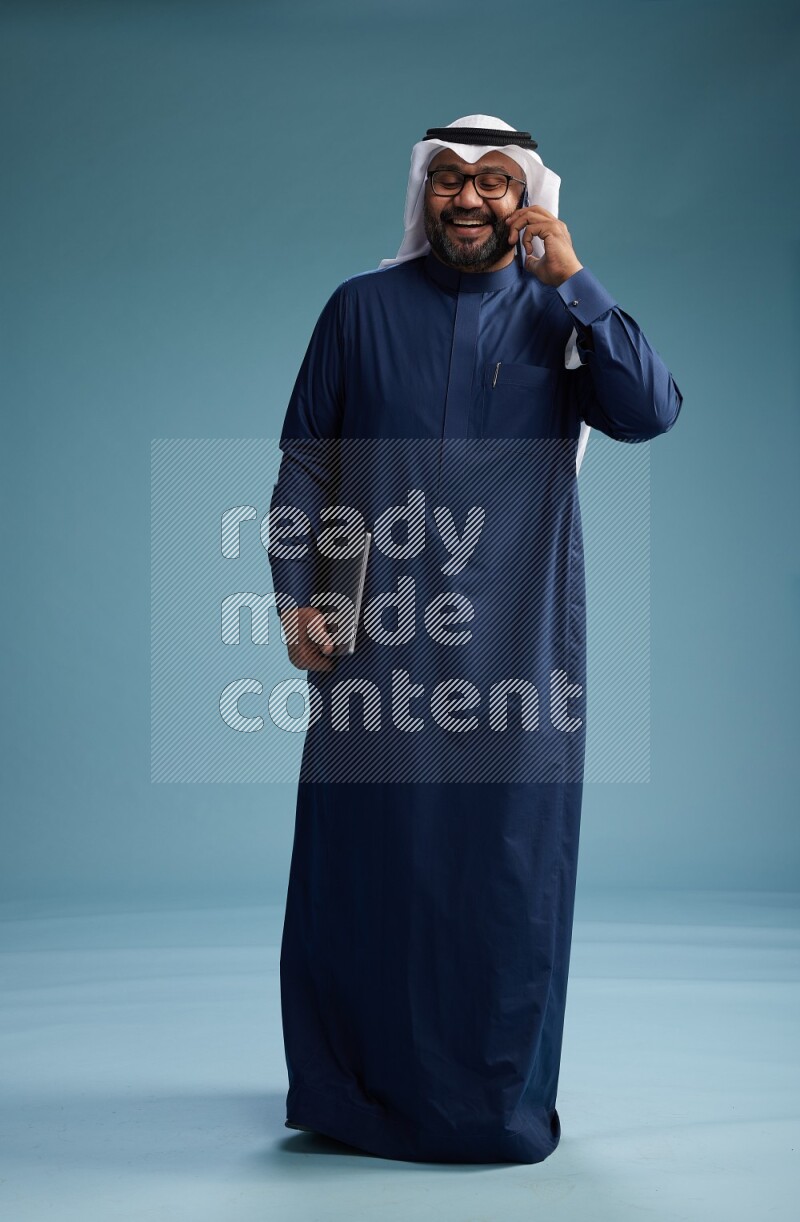 Saudi Man with shimag Standing talking on phone on blue background