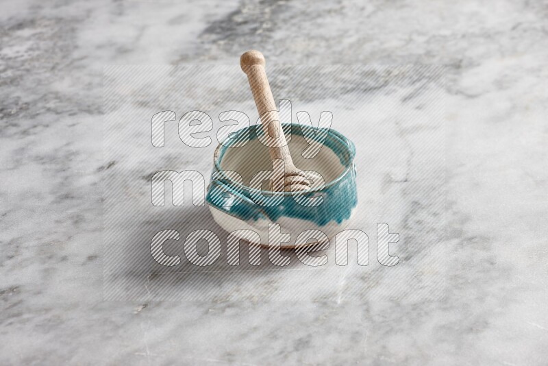 Multicolored pottery bowl with wooden honey dipper in it on grey marble background