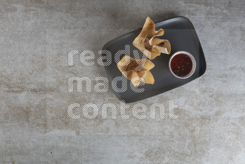 wonton cups with soy sauce ramkin on rectangle dark grey ceramic plate on grey textured counter top