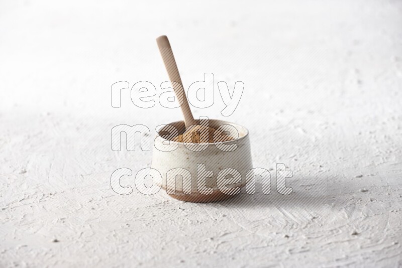 Ceramic beige bowl full of cinnamon powder with a wooden spoon on a textured white background