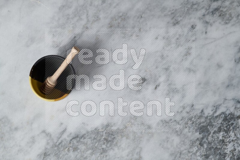 Multicolored pottery bowl with wooden honey dipper in it on grey marble background