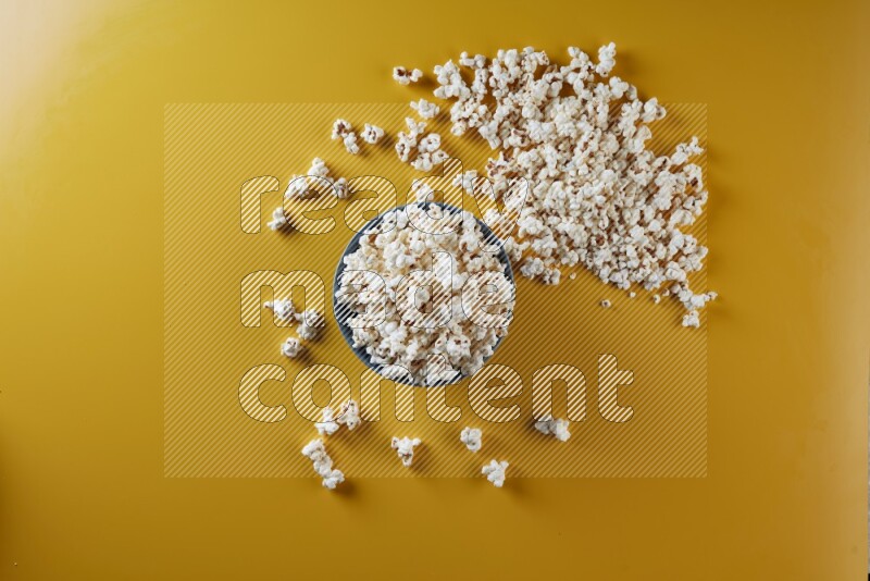 A blue pottery bowl full of popcorn with popcorn beside it on a yellow background in different angles