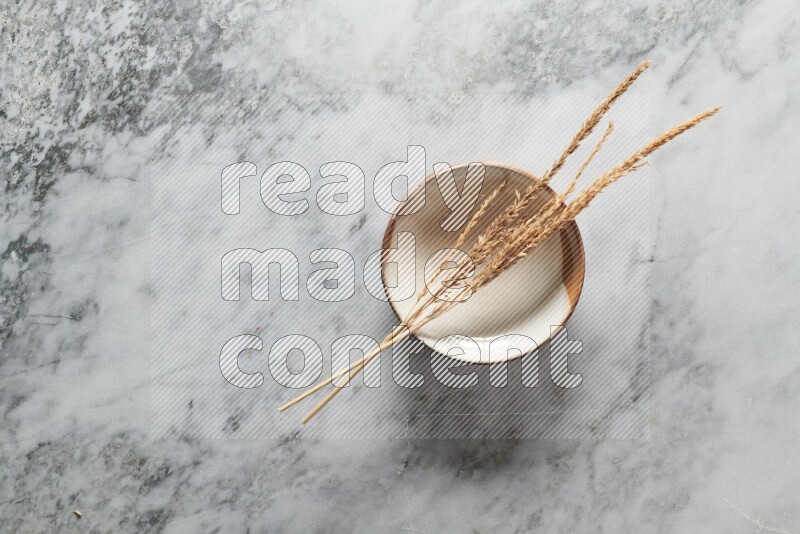 Wheat stalks on multicolored pottery plate on grey marble background