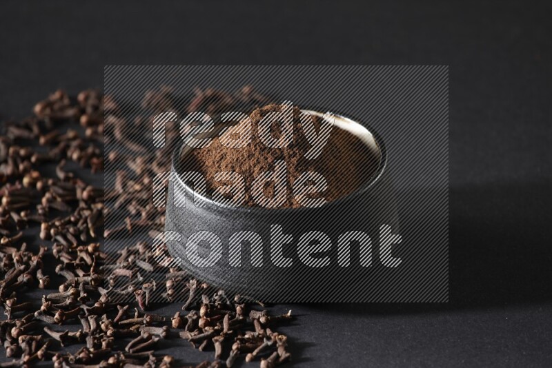 وعاء فخاري أسود ممتلئ ببودرة القرنفل وحبوب القرنفل على خلفية سوداء