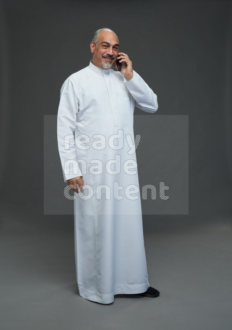 Saudi man without shomag Standing talking on phone on gray background