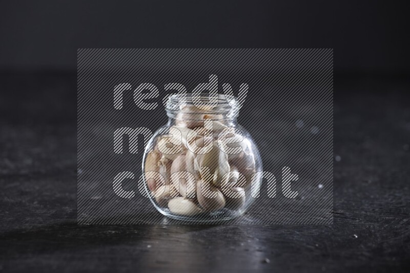 A glass spice jar full of garlic cloves on a textured black flooring