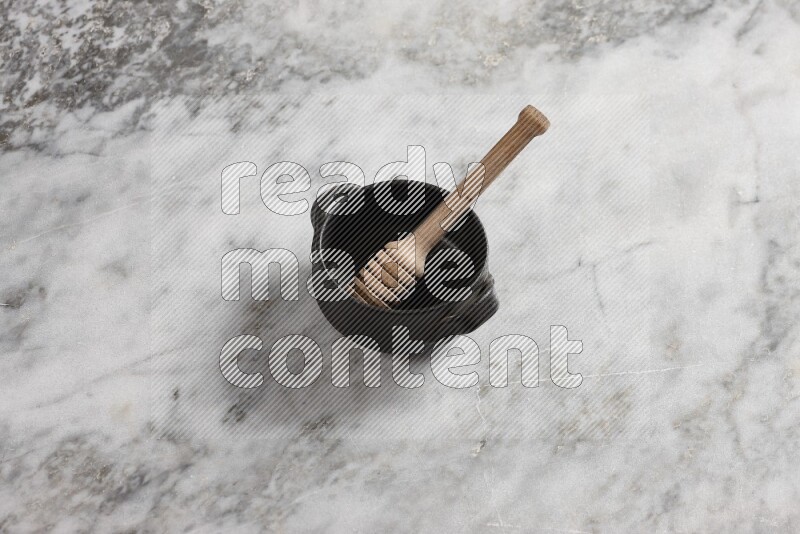 Black pottery bowl with wooden honey dipper in it on grey marble background