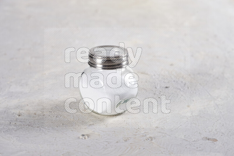 A glass jar full of fine table salt on white background