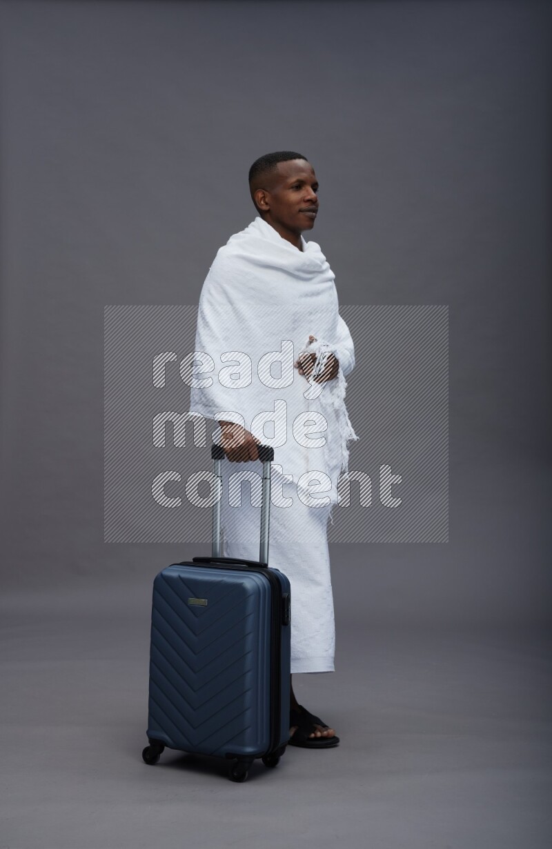 A man wearing Ehram Standing holding traveling bag on gray background