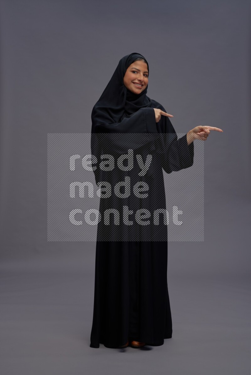 Saudi woman wearing Abaya standing interacting with the camera on gray background