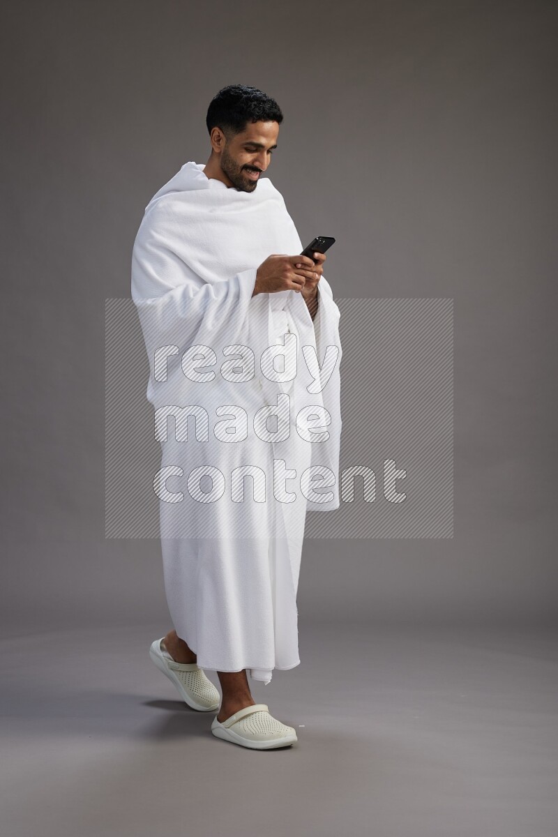 A man wearing Ehram Standing texting on phone on gray background
