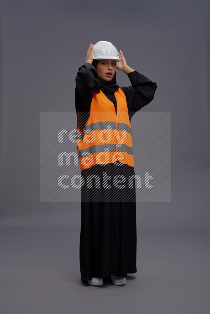 Saudi woman wearing Abaya with engineer vest standing interacting with the camera on gray background