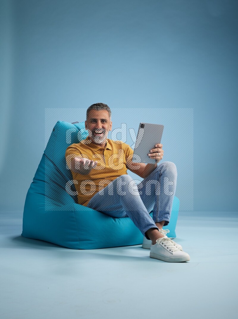 A man sitting on a blue beanbag and working on tablet