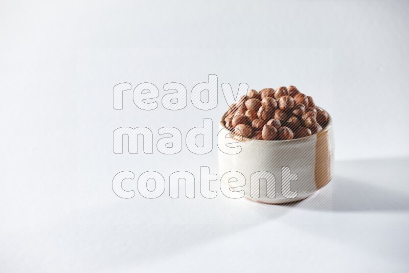 A beige ceramic bowl full of peeled hazelnuts on a white background in different angles